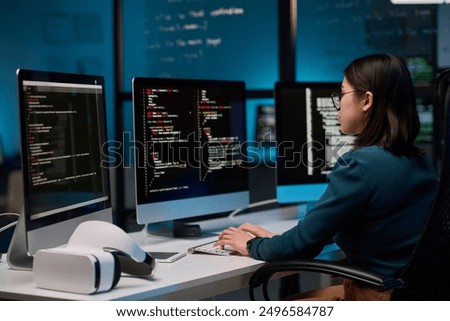 Female IT developer writing code for VR project at office workplace with focus on computer screens copy space