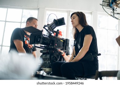 Female Director Of Photography With A Camera On A Movie Set. Professional Videographer On The Set Of A Movie, Commercial Or TV Series. Filming Indoors, Studio