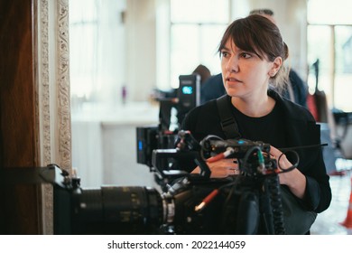 Female Director Of Photography With A Camera On A Movie Set. Professional Videographer On The Set Of A Movie, Commercial Or TV Series. Filming Indoors, Studio