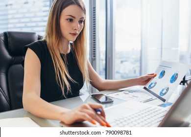 Female director working in office sitting at desk analyzing business statistics holding diagrams   charts using laptop