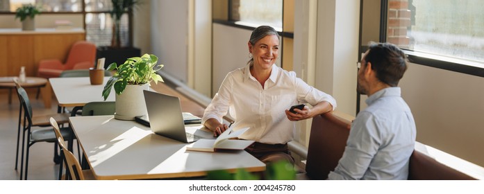 Female discussing new project with male colleague. Mature woman talking with young man in office. - Shutterstock ID 2004245780
