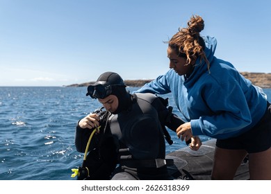 Instructor de buceo femenino que ayuda al buceador masculino que prepara el equipo de buceo en el barco inflable en el mar