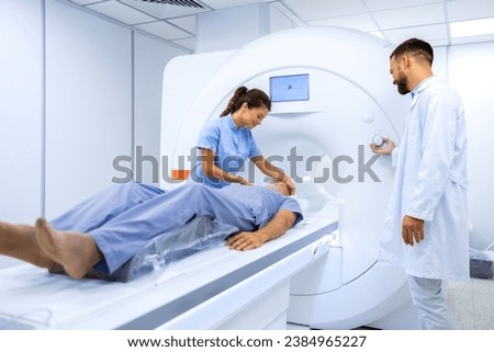 Female doctor assisting senior patient while doing MRI scan in medical examination room.