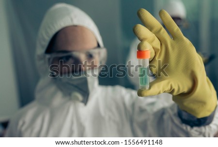 Female doctor with baceriological protective suit looking at an antidote vial for a dangerous virus