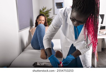 Female doctor bandaging a smiling young patient's injured ankle in a medical office - Powered by Shutterstock