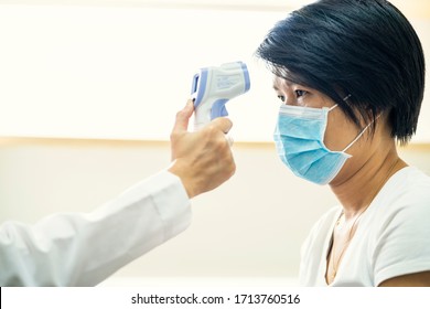 Female Doctor Check Asian Woman Body Temperature Using Infrared Forehead Thermometer (thermometer Gun) For Virus Symptom At Hospital. Corona Virus, Covid-19, Quarantine Or Virus Outbreak Concept