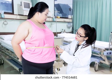 Female doctor checking belly of obese woman with measuring tape in the patient room