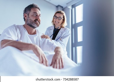 Female Doctor Checking Male Patient. Doctor Visiting And Talking With Patient Sitting In A Hospital Bed.