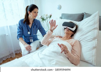 Female Doctor Checking on Elderly Patient Lying in Hospital Bed Doing Therapy Via VR Technology. Friendly Doctor Helping Senior Woman Receive Therapy Using Virtual Reality Headset. - Powered by Shutterstock