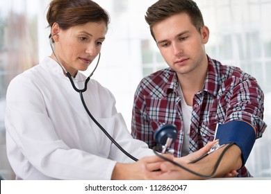 Female Doctor Checking Young Man Blood Pressure