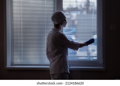 A Female Doctor Closes The Blinds On A Window In A Hospital, Rear View.