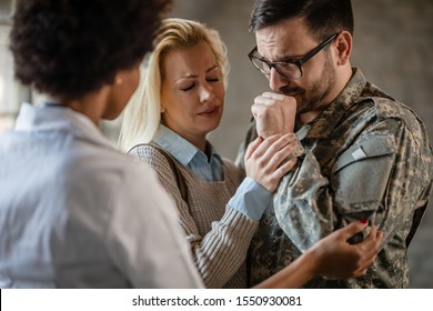 Female Doctor Comforting Crying Veteran And His Wife After Receiving Bad News At Medical Clinic. Focus Is On Soldier. 