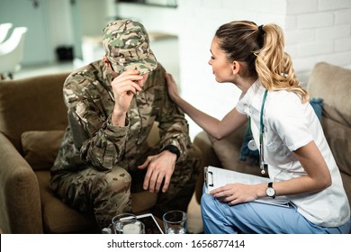 Female Doctor Comforting Sad Military Man While Visiting Him At Home. 