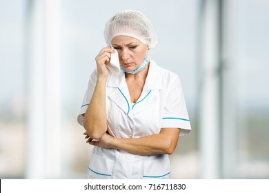 Female Doctor Crying, Blurred Background. Beautiful Mature Doctor In White Uniform Looking Worried And Cry.