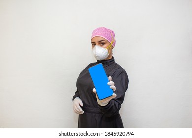 Female Doctor Or Dentist In Surgical Suit And N95 Face Mask Showing Cell Phone Screen