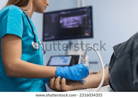 Female doctor doing ultrasound examination of patient's arm veins in her office. Young man passing ultrasound scan in clinic. Doctor work. Medical research.
