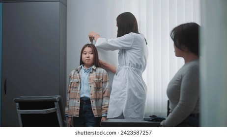 Female doctor, endocrinologist weighs and measures height of Asian girl in hospital office. Young patient undergoes examination or does checkup in modern clinic. Concept of medicine and healthcare. - Powered by Shutterstock