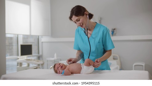 Female Doctor Examining Baby With Stethoscope In Clinic. Woman Pediatrician In Scrubs Listening To Newborn Baby Heartbeat With Stethoscope During Checkup In Hospital