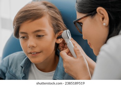 Female doctor examining boy's ear with otoscope. Ear cavity treatment health checkup. Barotrauma, pressure, otitis, laryngitis concept. - Powered by Shutterstock