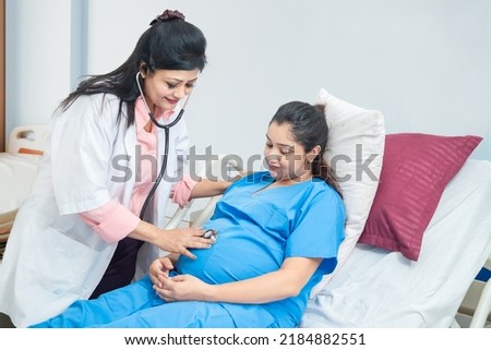 Female Doctor Examining Indian Pregnant Woman Holding Stethoscope Near Belly Listening Baby's Heartbeat at hospital or clinic . Pregnancy Checkup.