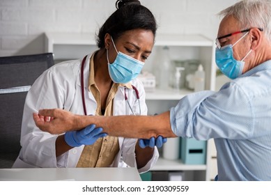 Female Doctor Is Examining Male Elderly Patient At Clinic. Doctor And Patient Wearing A Face Mask.