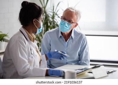 Female Doctor Is Examining Male Elderly Patient At Clinic. Doctor And Patient Wearing A Face Mask.