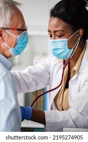 Female Doctor Is Examining Male Elderly Patient At Clinic. Doctor And Patient Wearing A Face Mask.