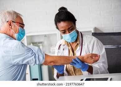 Female Doctor Is Examining Male Elderly Patient At Clinic. Doctor And Patient Wearing A Face Mask.
