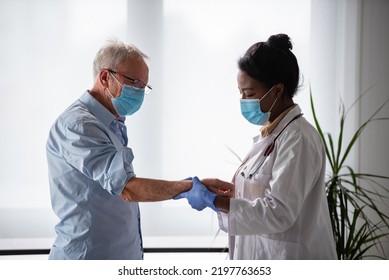 Female Doctor Is Examining Male Elderly Patient At Clinic. Doctor And Patient Wearing A Face Mask.
