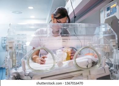 Female doctor examining newborn baby in incubator. Night shift