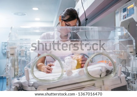 Female doctor examining newborn baby in incubator. Night shift