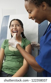 Female Doctor Examining Teenage Girl With Tongue Depressor In Clinic