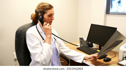 Female doctor examining an x-ray while talking on telephone at the hospital - Powered by Shutterstock