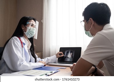 Female Doctor Explain X-ray Chest Result In Computer Laptop To Illness Man Patient In Examination Room In Hospital. Female Medic Wear Face Shield And Mask During Covid Pandemic To Prevent Infection.