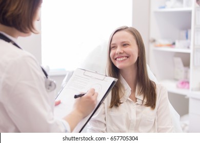 Female Doctor Explaining Diagnosis To Her Female Patient With Happy Smile And Taking Notes