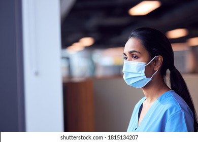 Female Doctor In Face Mask Wearing Scrubs Under Pressure In Busy Hospital During Health Pandemic