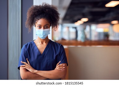 Female Doctor In Face Mask Wearing Scrubs Under Pressure In Busy Hospital During Health Pandemic