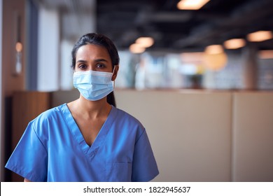 Female Doctor In Face Mask Wearing Scrubs Under Pressure In Busy Hospital During Health Pandemic