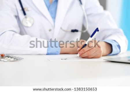 Female doctor filling up prescription form while sitting at the desk in hospital closeup.  Healthcare, insurance and excellent service in medicine concept 