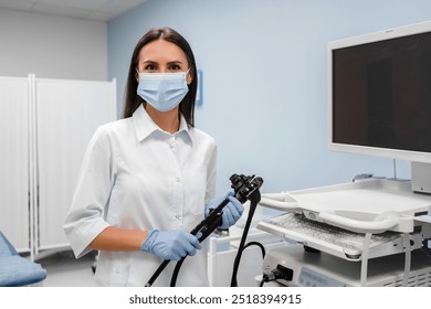 Female doctor gastroenterologist with probe to perform gastroscopy and colonoscope in white lab coat protective gloves and facial mask looking at camera. Gastrointestinal fiberoptic endoscopy concept. - Powered by Shutterstock