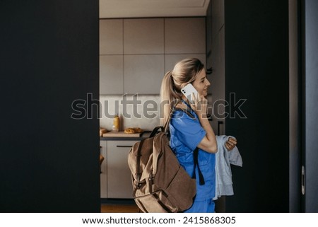 Female doctor getting ready for work, reading message on smartphone, leaving house in scrubs with backpack. Work-life balance for healthcare worker.