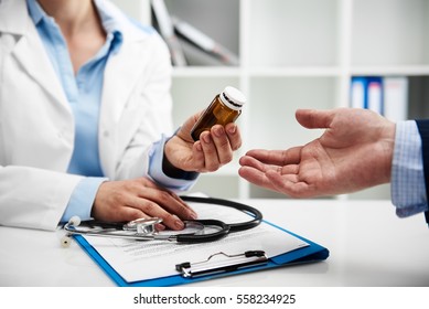 Female doctor giving pills bottle to male patient in clinic. Concept of healthcare, medical treatment and insurance.