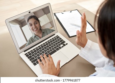 Female doctor gp consulting indian woman patient make online webcam video call on laptop screen. Telemedicine conference remote computer virtual visit in zoom meeting. Over shoulder videocall view.
