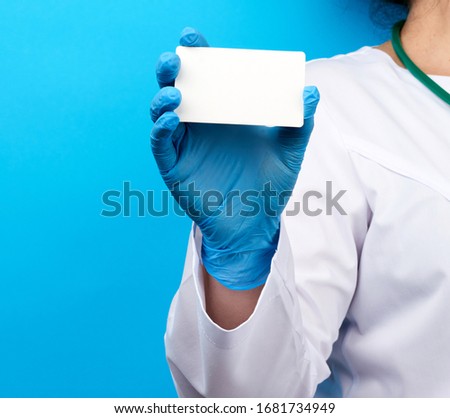 female doctor hand in blue medical latex gloves holds an empty paper business card on a blue background, place for an inscription
