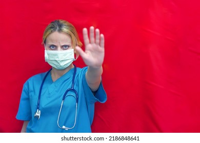 Female Doctor Hand Gesturing STOP. Doctor With Stop Hand. Woman Doctor In Blue Uniform Show Hand Up Stop Sign, Studio Shot Isolated Over Red Background, Medical Health Concept