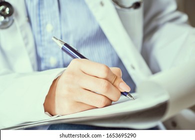 Female doctor hand hold silver pen filling patient history list at clipboard pad. Panacea and life save, prescribing treatment.