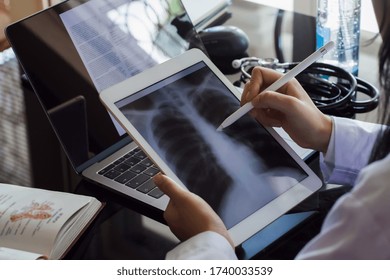 Female doctor hand holding digital tablet with chest x-ray film (CXR ) on screen and work on laptop computer at the office in clinic or hospital. Medical and health care concept. - Powered by Shutterstock