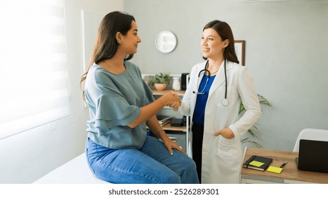 Female doctor happily shaking hands with her hispanic patient after a successful consultation in her office - Powered by Shutterstock