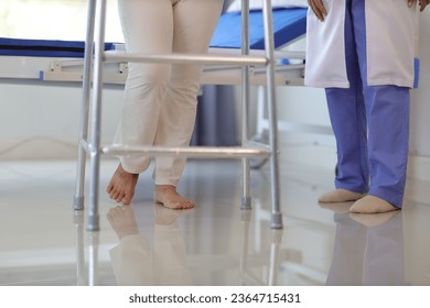 Female doctor help a senior patient who is doing physical therapy and is practicing walking with a walking stick. - Shutterstock ID 2364715431