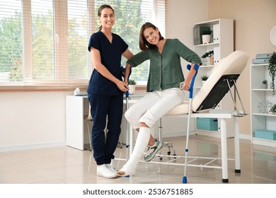 Female doctor helping woman with broken leg and crutches to stand up from couch in clinic - Powered by Shutterstock